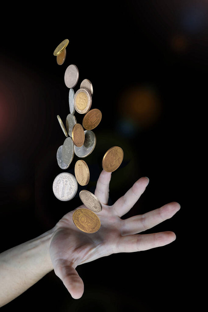 Hand gooien van verschillende geld munten op wazig donkere achtergrond, selectieve focus - Foto, afbeelding