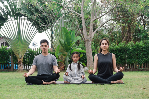 la joven familia está haciendo yoga en el parque, están sentados en pose de loto y meditando  - Foto, Imagen