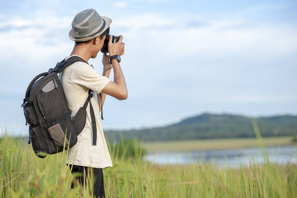Jonge Aziatische man reiziger draagt gebreide hoed met rugzak het nemen van een foto bij geweldig meer. Reizen vakantie ontspanning concept - Foto, afbeelding