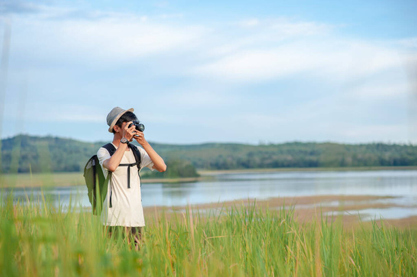 Jovem asiático viajante vestindo chapéu de malha com mochila tirando uma foto no lago incrível. Viagem férias relaxamento conceito - Foto, Imagem