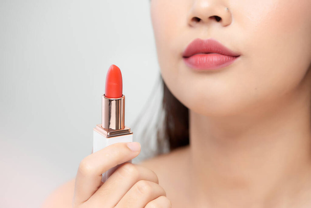 Beautiful young asian woman holding lipstick over white background - Photo, Image