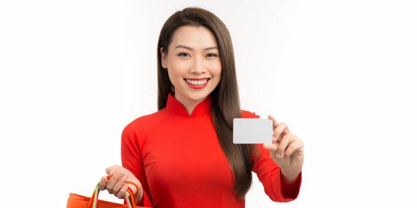 Asian woman in ao dai traditional red dress holding shopping bag and paid via credit in Lunar New Year Festival - Photo, Image