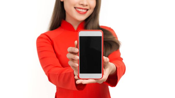 Közelkép portré egy mosolygó ázsiai nő mutatja üres képernyős mobiltelefon, miközben áll elszigetelt fehér backgrou - Fotó, kép
