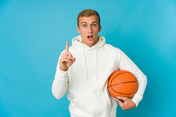 Basketbol oynayan beyaz bir adam mavi arka planda izole edilmiş. Bir fikri, ilham verici bir fikri var.. - Fotoğraf, Görsel