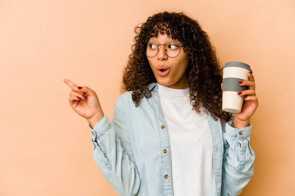 Junge afrikanisch-amerikanische Afro-Frau hält einen Kaffee zum Mitnehmen und zeigt zur Seite - Foto, Bild