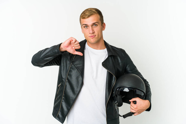 Joven hombre caucásico sosteniendo un casco de moto aislado sobre fondo blanco mostrando un gesto de aversión, pulgares hacia abajo. Concepto de desacuerdo. - Foto, imagen