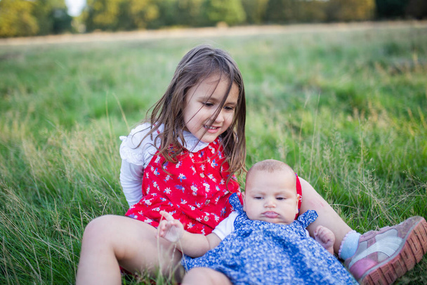 Schattig klein meisje en baby liggend op het gras - Foto, afbeelding