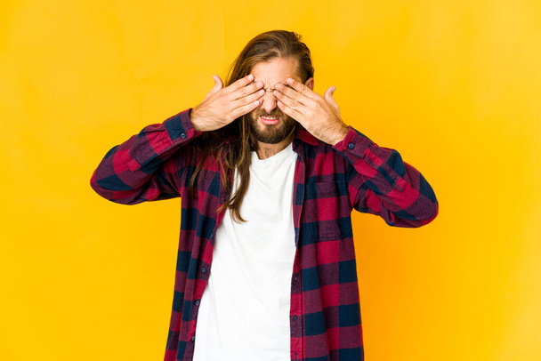 Young man with long hair look afraid covering eyes with hands. - Foto, afbeelding