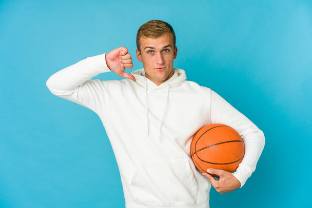 Nuori valkoihoinen mies pelaa koripalloa eristetty sinisellä taustalla seisoo ojennettu käsi osoittaa stop-merkki, estää sinua. - Valokuva, kuva