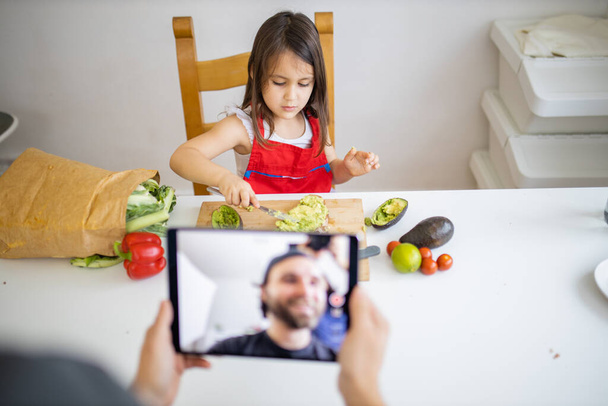 Homem gravando com um tablet enquanto sua filhinha corta um abacate - Foto, Imagem