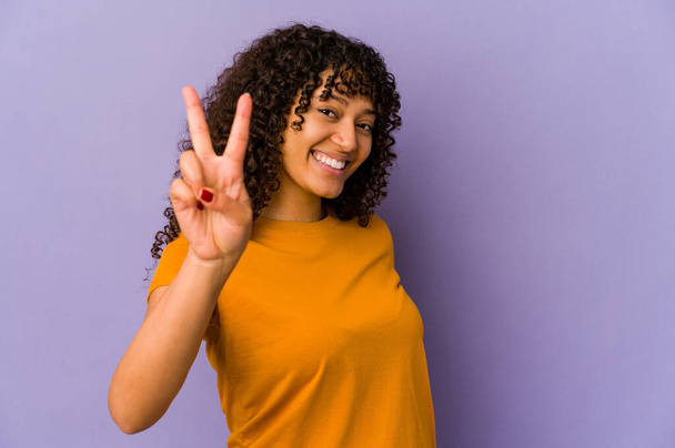 Joven afroamericana afro mujer aislada alegre y despreocupada mostrando un símbolo de paz con los dedos. - Foto, imagen