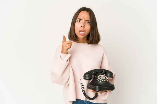 Молода іспаномовна жінка тримає старовинний телефон ізольовано, маючи ідею, концепцію натхнення
. - Фото, зображення