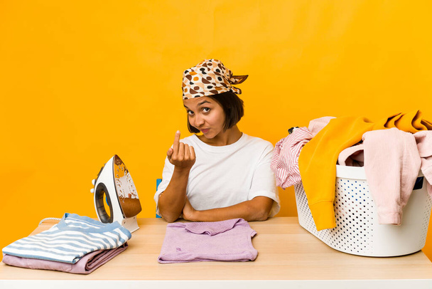 Young hispanic woman ironing clothes isolated pointing with finger at you as if inviting come closer. - Photo, Image