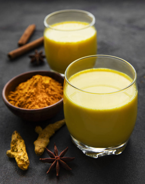 Yellow turmeric latte drink. Golden milk with cinnamon, turmeric, ginger  and honey over black stone background. - Фото, зображення