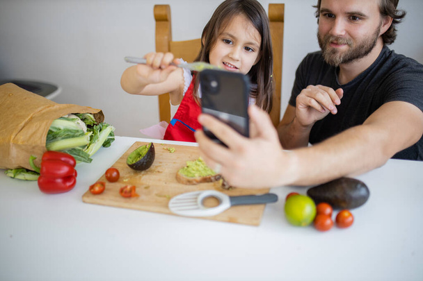 Vader en dochter nemen een selfie tijdens het maken van avocado toast - Foto, afbeelding