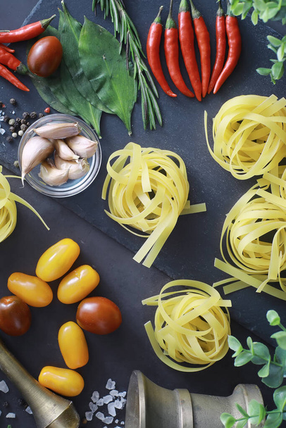Pasta on the table with spices and vegetables. Noodles with vegetables for cooking on black stone background. - Foto, imagen