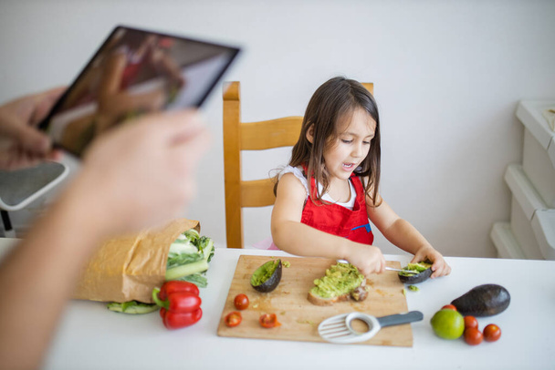 Mãos masculinas com um tablet gravando uma menina cortando um abacate - Foto, Imagem