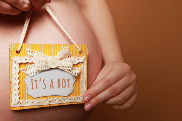 Egy terhes nő egy táblát tart a hasa mellett sárga alapon. - Fotó, kép
