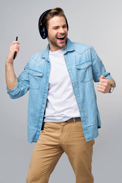 Close up portrait of cheerful young man enjoying listening to music wearing casual jeans outfit - Fotó, kép