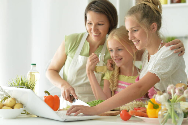 Cute girls with mother  cooking and looking at laptop   in kitchen - Foto, afbeelding