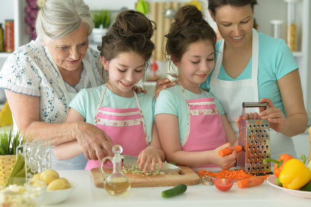 Cute girls with mother and grandmother   preparing delicious fresh salad in kitchen - Foto, afbeelding