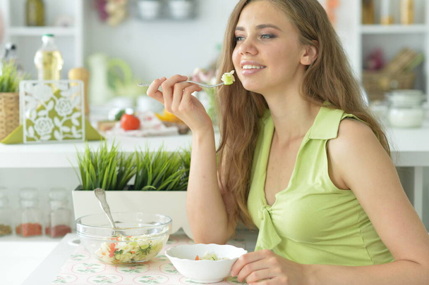 beautiful young woman eating salad in kitchen - Foto, Imagen