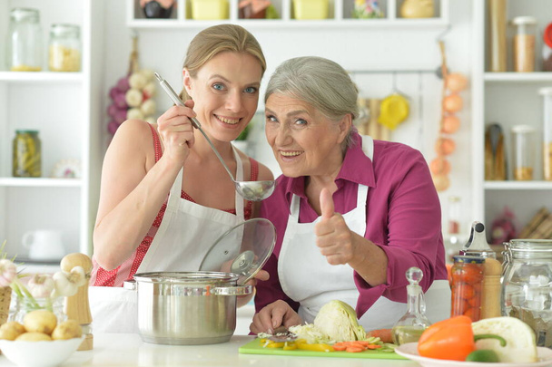 Smiling senior mother and adult daughter cooking together at kitchen - Foto, Bild