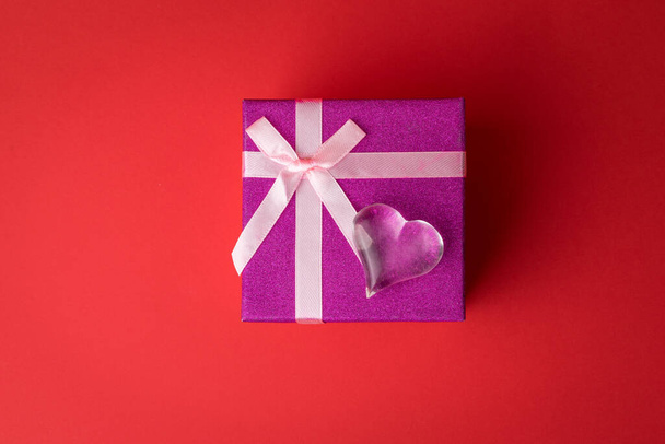 Glass heart at the top of a gift box on a red background. A Declaration of love. - Zdjęcie, obraz