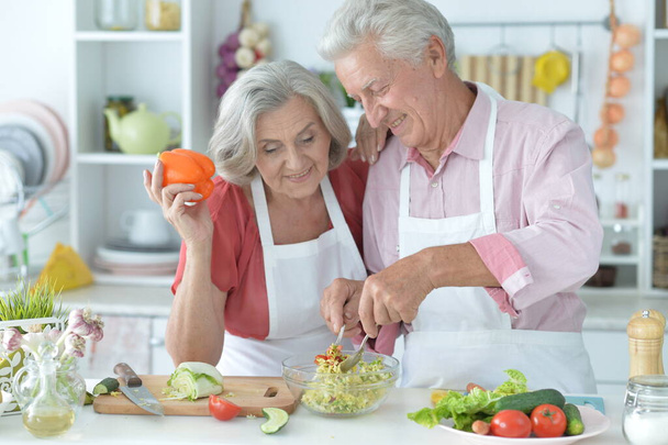 happy senior couple making salad together at kitchen - Фото, изображение