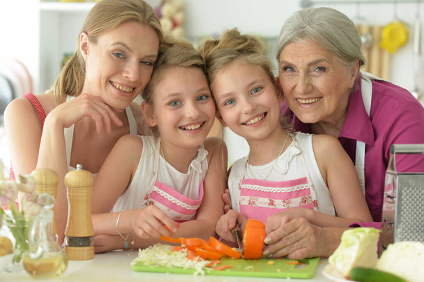 Cute girls with mother and grandmother preparing delicious fresh salad in kitchen - Foto, Imagem