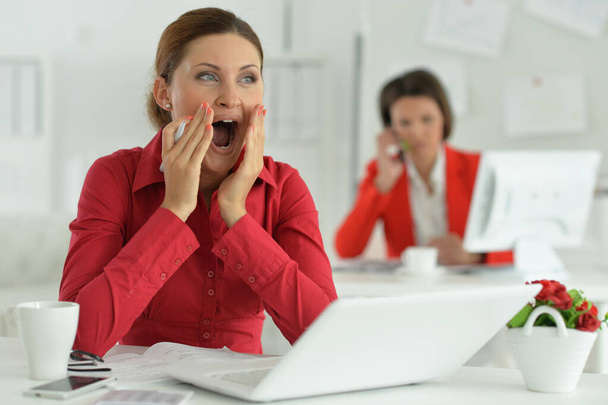 yawning businesswoman architect working in modern office with her colleague on background - Foto, imagen