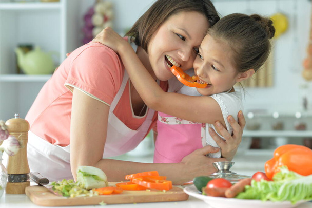 Cute little girl with her mother cooking together at kitchen table  - Foto, immagini