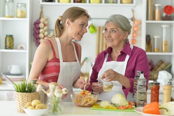 Smiling senior mother and adult daughter cooking together at kitchen - Photo, image