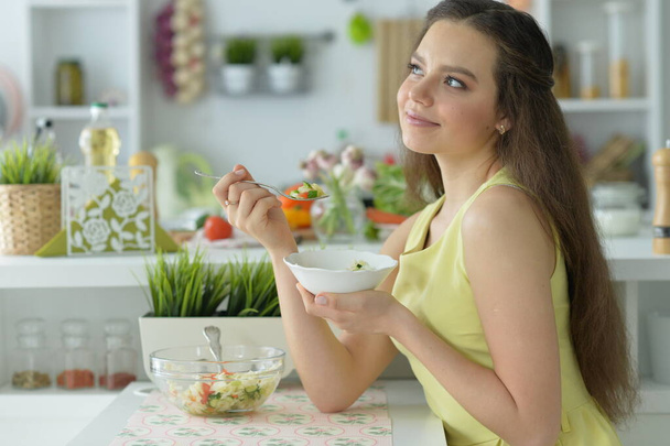 schöne junge Frau isst Salat in der Küche - Foto, Bild