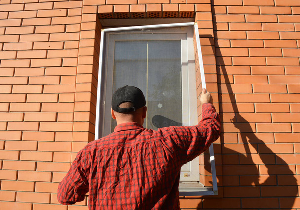 Člověk instaluje účinnou ochranu proti hmyzu, síť proti komárům na okně domu, aby se zbavil much, brouků a komárů.. - Fotografie, Obrázek