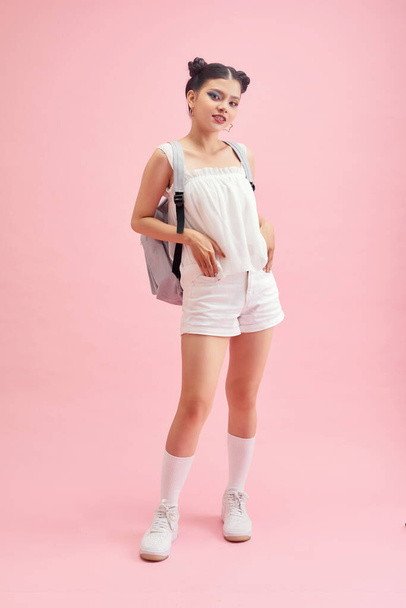 Divatos fiatal lány visel holding hátizsák, pózol elszigetelt rózsaszín háttér. - Fotó, kép