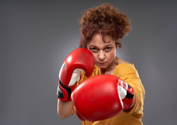 Senior woman trying out boxing with red gloves, isolated on gray background - Foto, Imagem