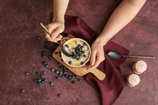 Woman eating tasty oatmeal with blueberry in bowl on table - Foto, Imagem