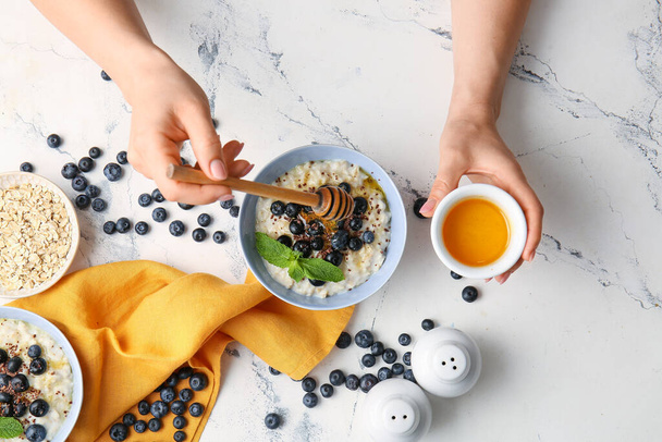 Woman putting honey in bowl with tasty oatmeal and blueberry on table - Fotó, kép