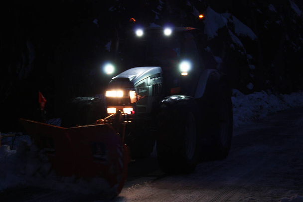 pług śnieżny przechodzi ze światłami przez śnieżne górskie uliczki wieczorem, aby oczyścić ruch drogowy - Zdjęcie, obraz
