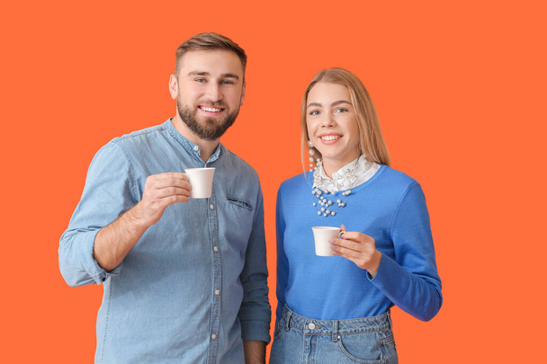 Mladý pár s horkou kávou na barevném pozadí - Fotografie, Obrázek