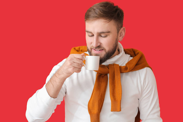 Schöner junger Mann mit heißem Kaffee auf farbigem Hintergrund - Foto, Bild