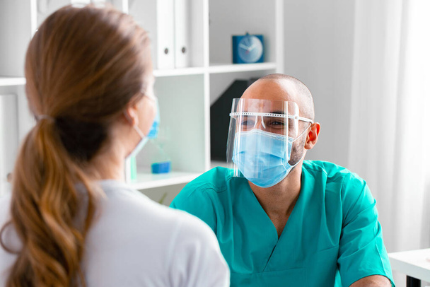 Arzt mit Gesichtsmaske spricht Patientin in Klinik an - Foto, Bild