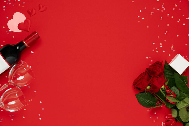 Modèle de Saint-Valentin plat laïc. Bouteille de vin, verres, fleurs roses avec boîte cadeau sur fond rouge - Photo, image