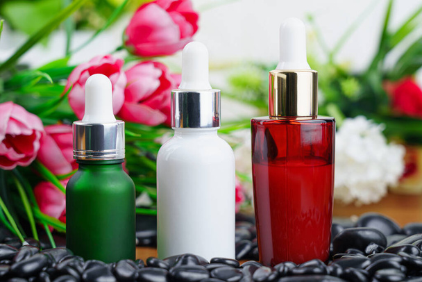 Tajski Spa ustawienie masażu z butelką oleju serum kroplomierz makieta lub olejek eteryczny na czarny kamień na tle kwiatów - Zdjęcie, obraz