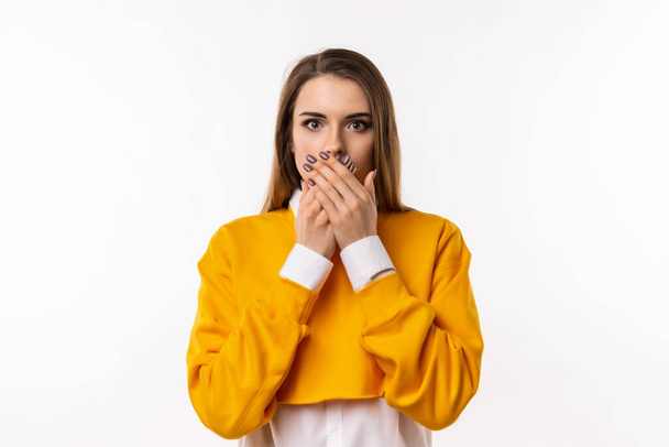 Frustrated brunette girl in casual clothes is covering mouth with two hands not willing to disclose something important. Keep a secret. Studio shot, white background - Foto, Imagem