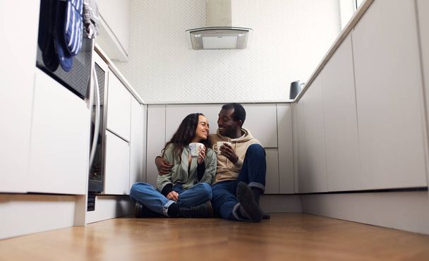 Nuori sekoitettu etnisyys pari juhlii muuttopäivää keittiössä istuu lattialla juoden kuumaa juomaa yhdessä - Valokuva, kuva
