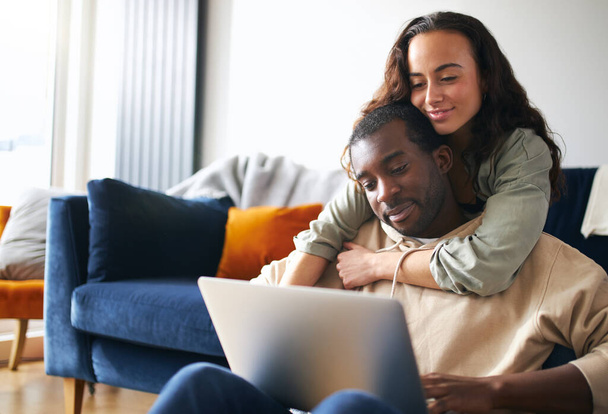 Nainen halaus mies takaapäin kuin nuori mixed etnisyys pari rentoutua sohvalla kotona selaamassa internetiä kannettavalla tietokoneella - Valokuva, kuva