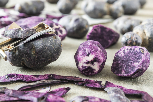 Pommes de terre violettes pelées et non pelées entières et coupées en deux sur fond gris - Photo, image