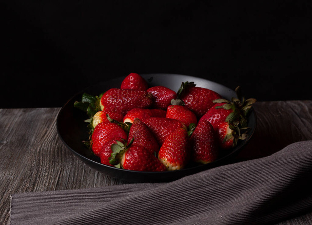 Bild eines Tellers Erdbeeren auf schwarzem Hintergrund horizontal. - Foto, Bild